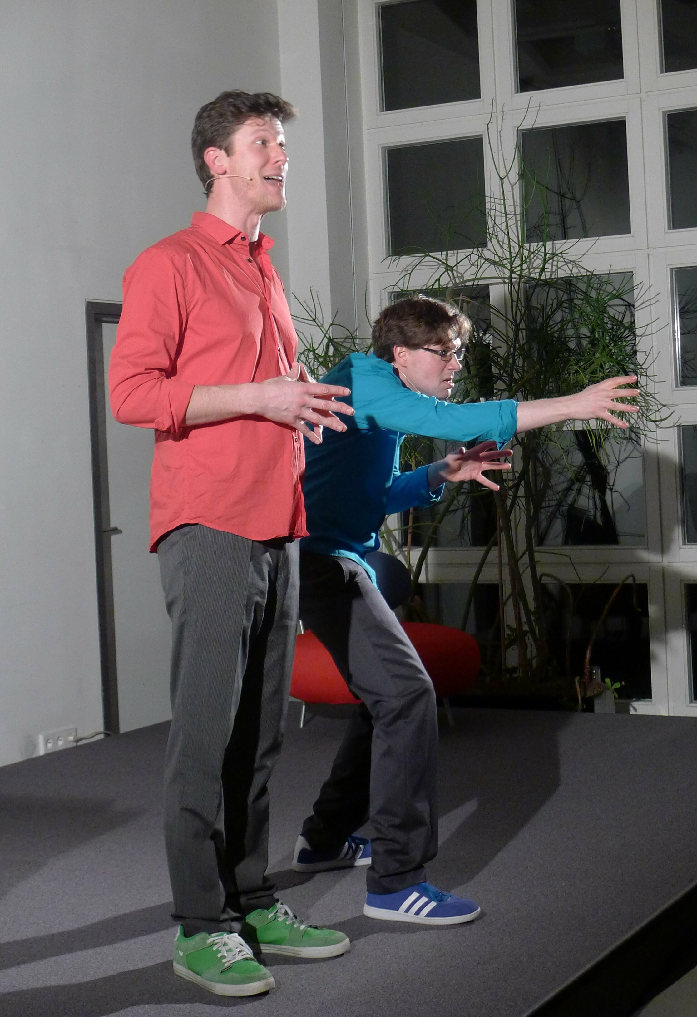 Das Foto zeigt lebendige Bühnenpoesie oder Geschichtenerzählen mit Ganzkörpereinsatz von Jakob Nacken (links) und Harry Kienzler (rechts).