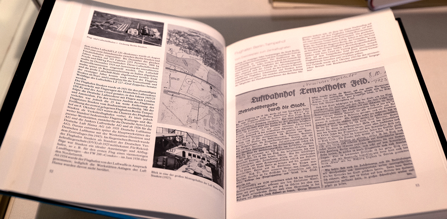 Geöffnetes Buch mit Schwarz-Weiß-Luftbildern, Landkarten und Zeitungsausschnitten
