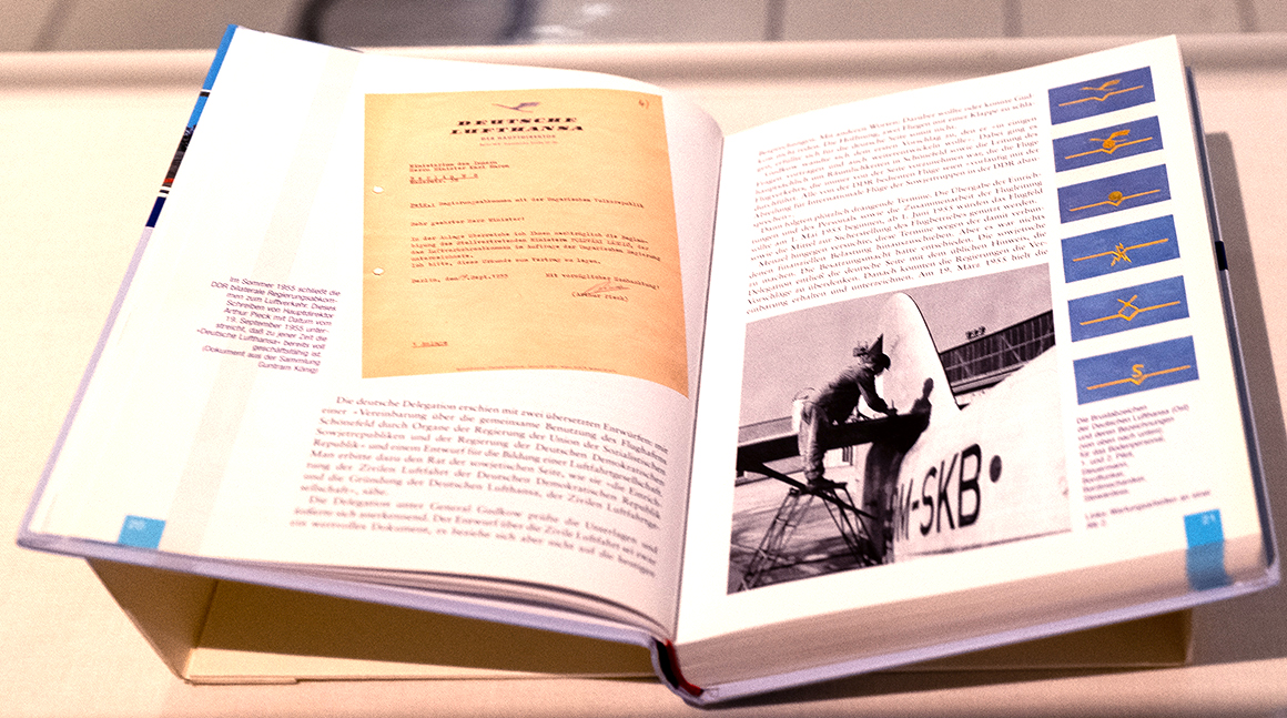 Geöffnetes Buch mit Darstellung eines Briefs der Deutschen Lufthansa, verschiedenen Abzeichen und einem Schwarz-Weiß-Foto eines Mannes an einem Flugzeug