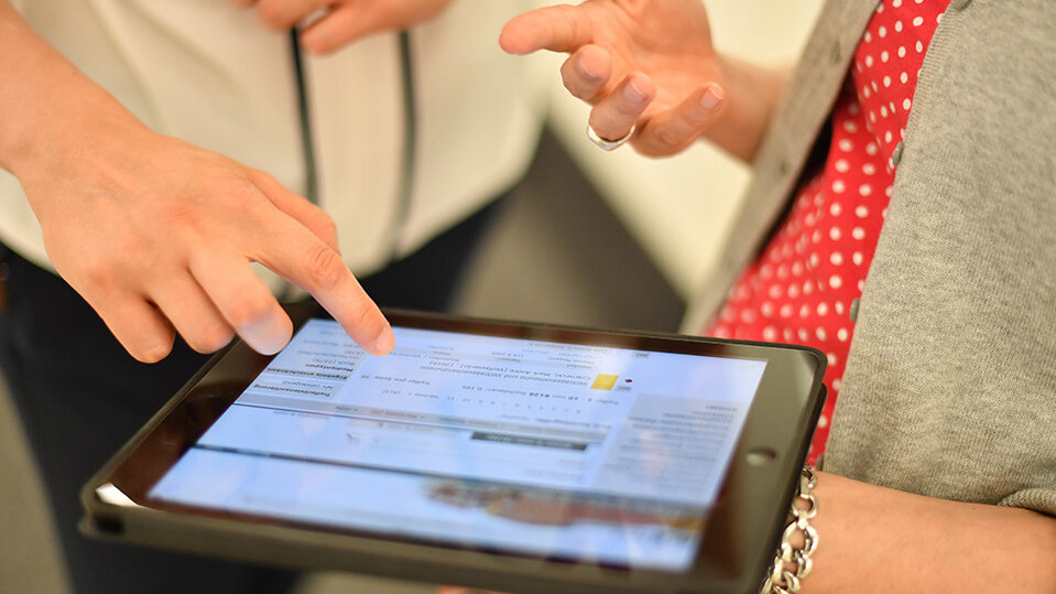 Eine Mitarbeiterin erklärt einer Benutzerin die E-Mail-Verwaltung auf einem Tablet.