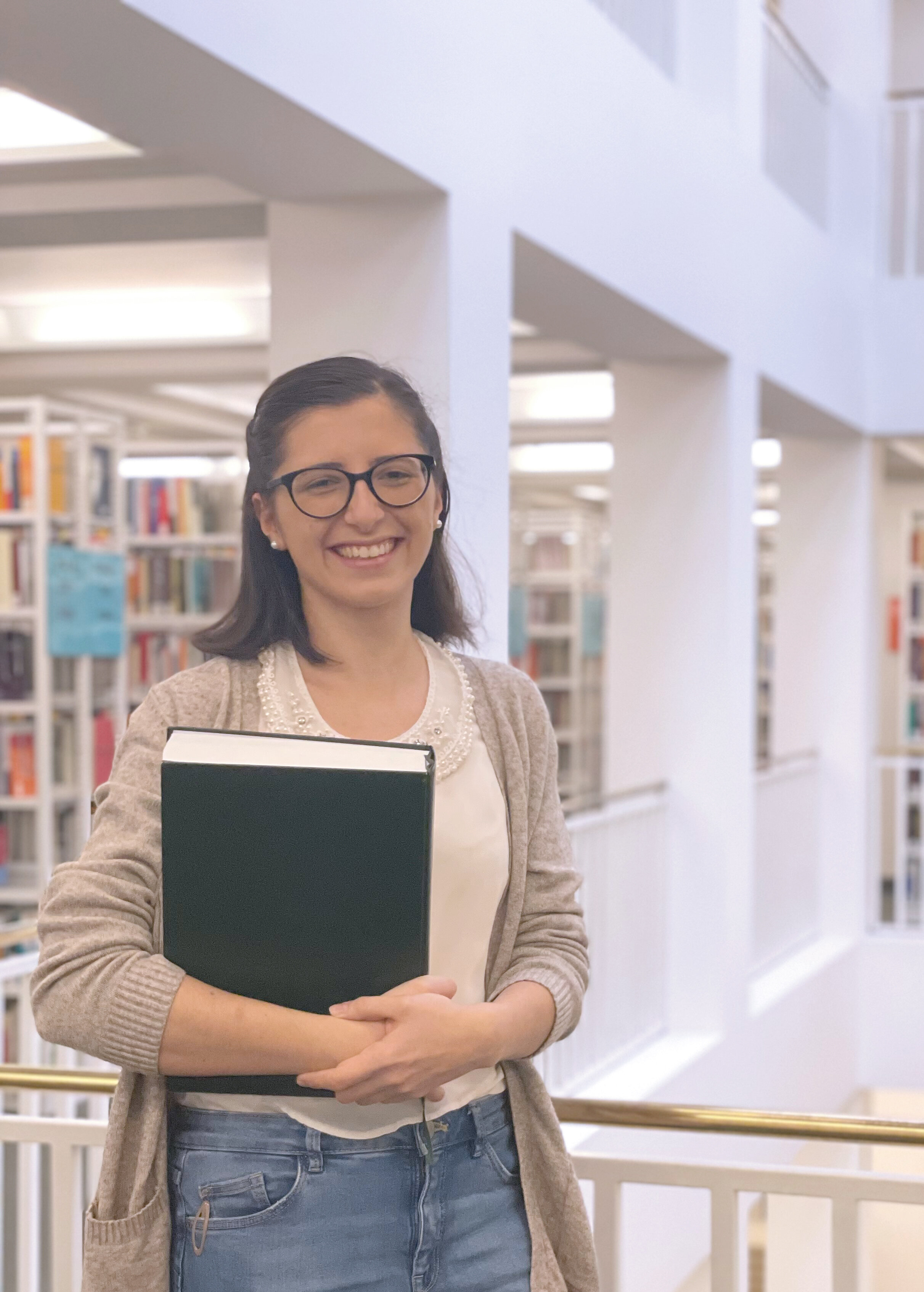 Das Bild zeigt eine junge Frau mit einem Buch in der Hand, die im Offenen Magazin der Badischen Landesbibliothek steht.