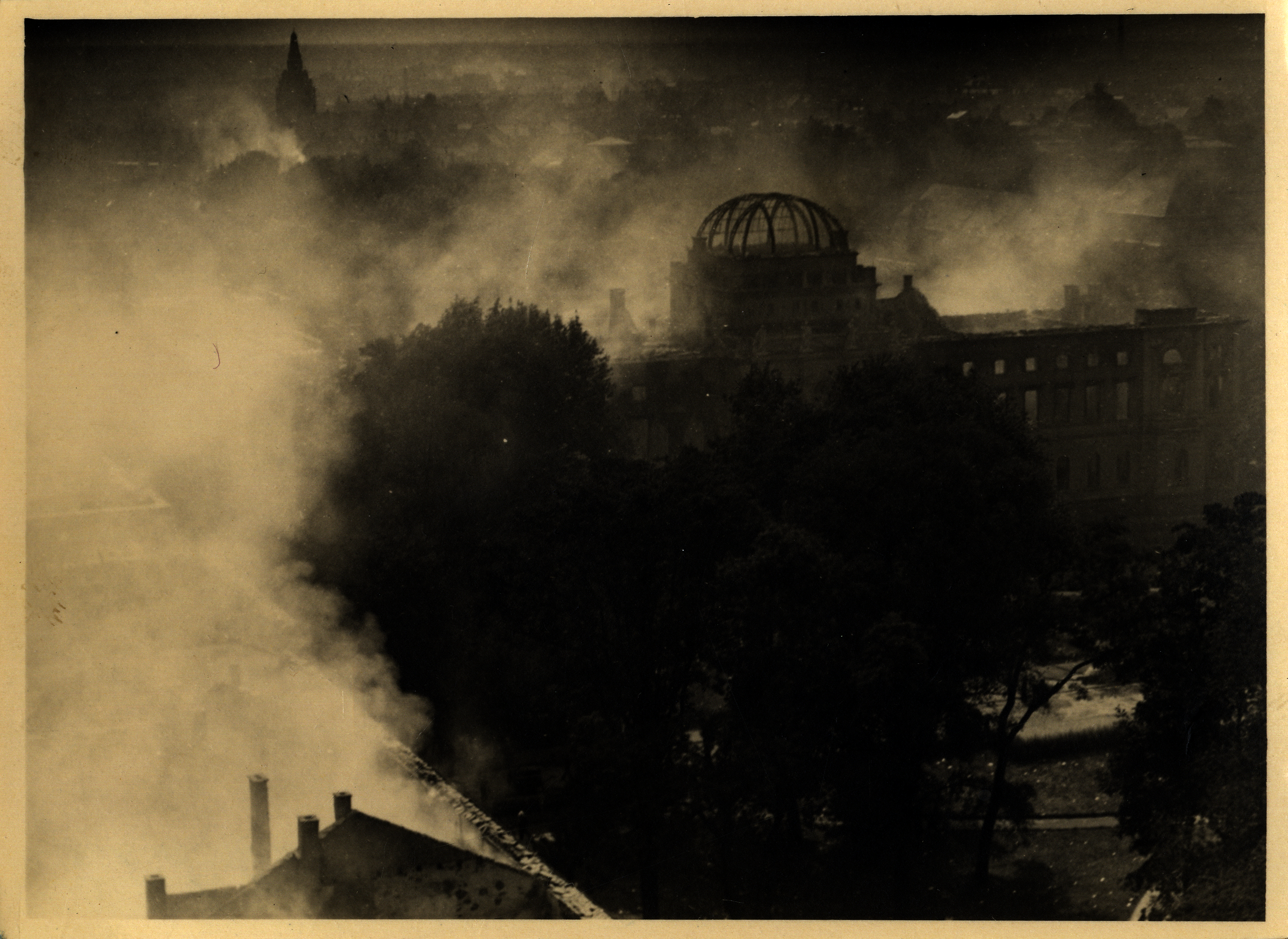 Die Fotografie aus der Bombennacht zeigt das brennende Sammlungsgebäude am Friedrichsplatz aus der Vogelperspektive, in Rauchschwaden gehüllt
