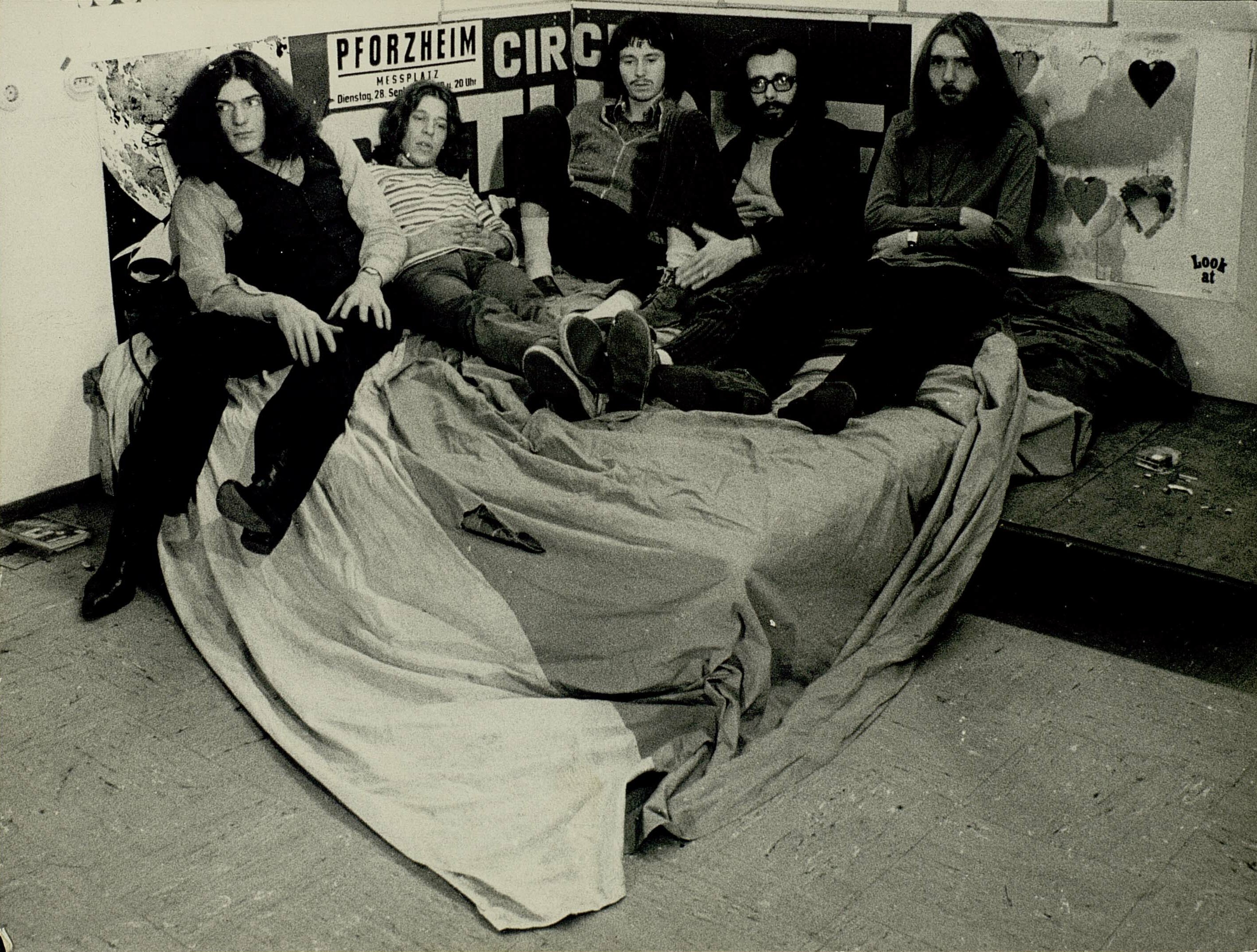 Schwarz-weiß Gruppenfoto der fünf Bandmitglieder von Checkpoint Charlie auf einem Bett.