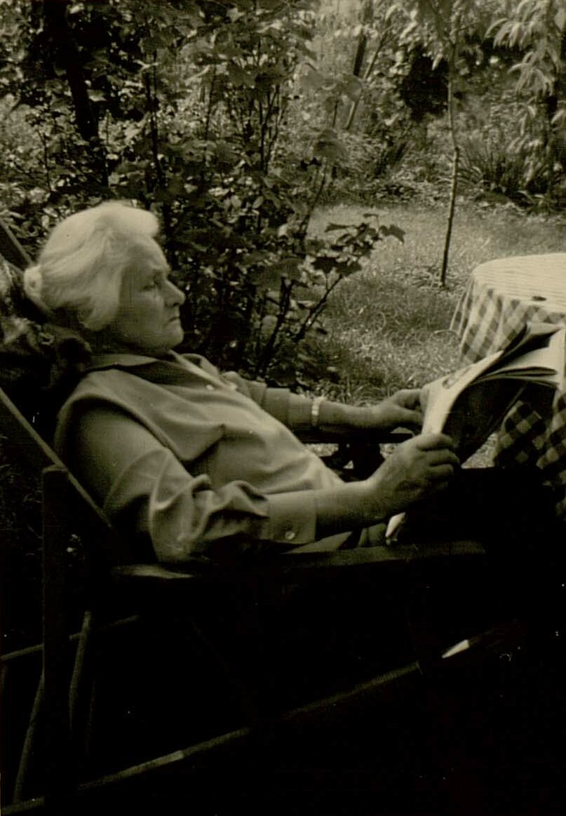 Foto von Elfriede Schork beim Lesen im Garten an einem Tisch mit karierter Tischdecke. Ihre weißen Haare sind in einen leichten Chignon gesteckt.