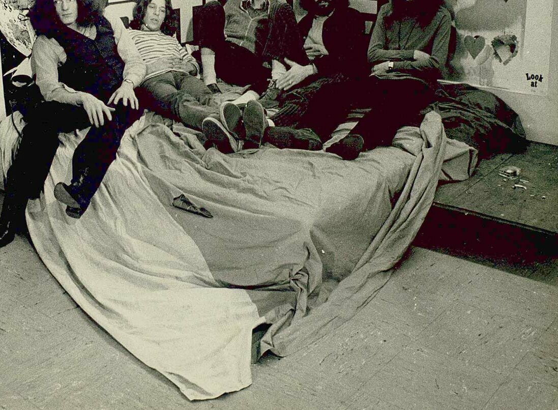 © Badische Landesbibliothek Schwarz-weiß Gruppenfoto der fünf Bandmitglieder von Checkpoint Charlie auf einem Bett.
