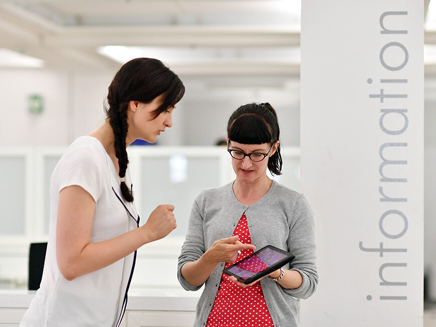 Zu sehen sind zwei Personen. Diese schauen auf ein Tablet. 