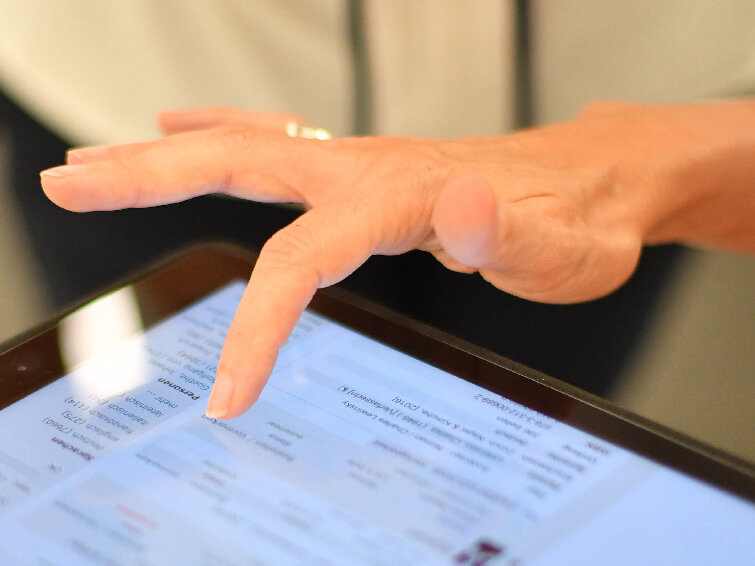 Das Bild ist eine Detailansicht einer Hand, deren Zeigefinger auf dem Bildschirm eines Tablets ein Werk aus der Ergebnisliste des Katalog plus auswählt. 
