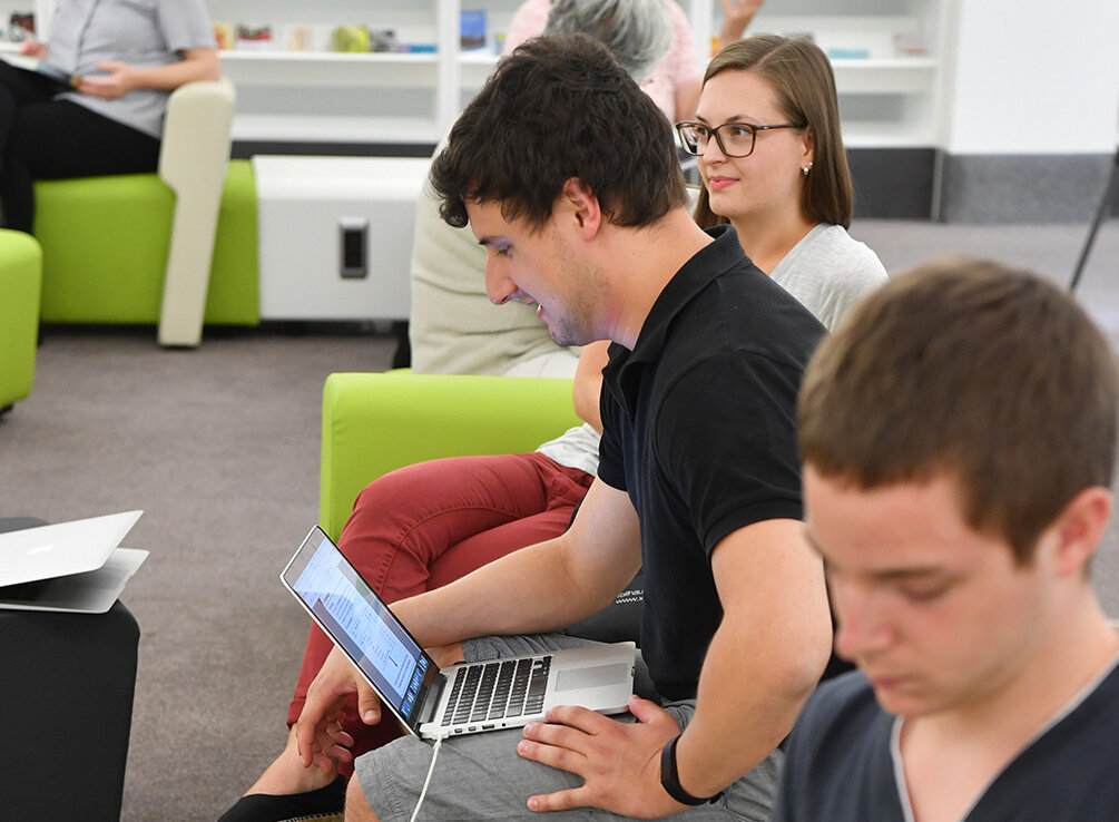 Zu sehen sind mehrere Personen mit Notebooks. Diese sitzen in der bibLounge der BLB. Das Motiv ist Hochformat aufgenommen, die Personen reihen sich linear als bildführende Diagonale auf. 