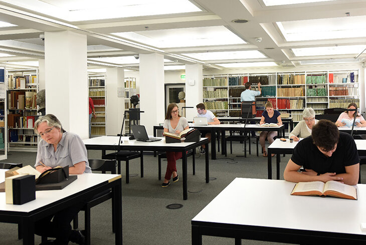 Das Bild zeigt Bibliotheksnutzerinnen und -nutzer, die an Arbeitsplätzen im Lesesaal Sammlungen der Badischen Landesbibliothek arbeiten.