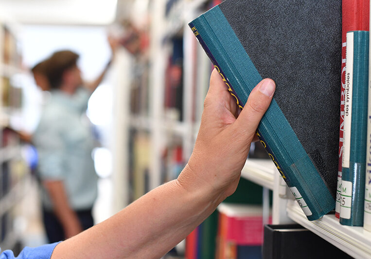 © Foto: Uli Deck Im Bild ist eine Hand zu sehen. Diese zieht ein Buch aus einem Bücherregal.