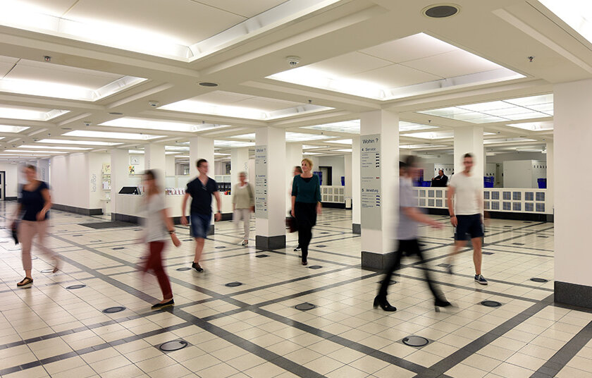 Zu sehen ist das Foyer der BLB. Zahlreiche Personen bewegen sich durch diesen Raum. Viele von Ihnen sind mit einer Bewegungsunschärfe fotografiert worden. 