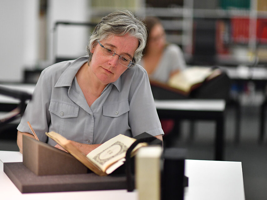 Das Bild zeigt eine Person mit einem aufgeschlagenen Buch um Lesesaal Sammlungen der BLB.