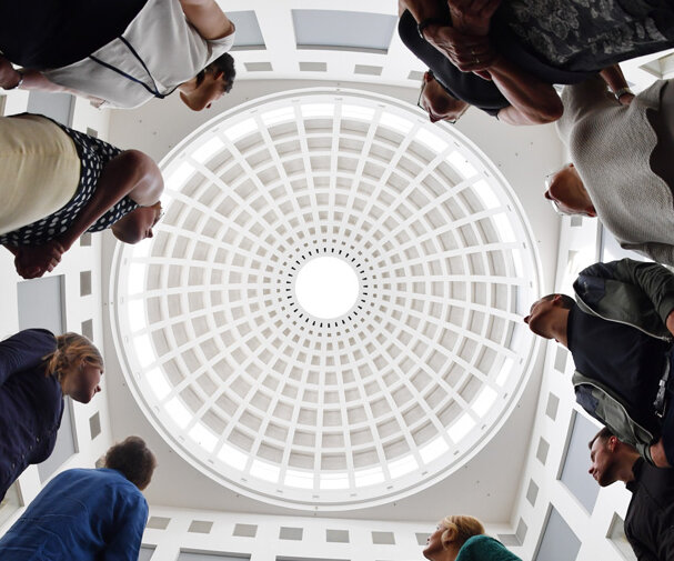 Das Bild zeigt eine Gruppe bei einer Führung durch den Lesesaal. Die Teilnehmerinnen und Teilnehmer blicken nach oben. Das Bild ist in extremer Untersicht aufgenommen, die Kuppel des Lesesaals ist zu sehen.