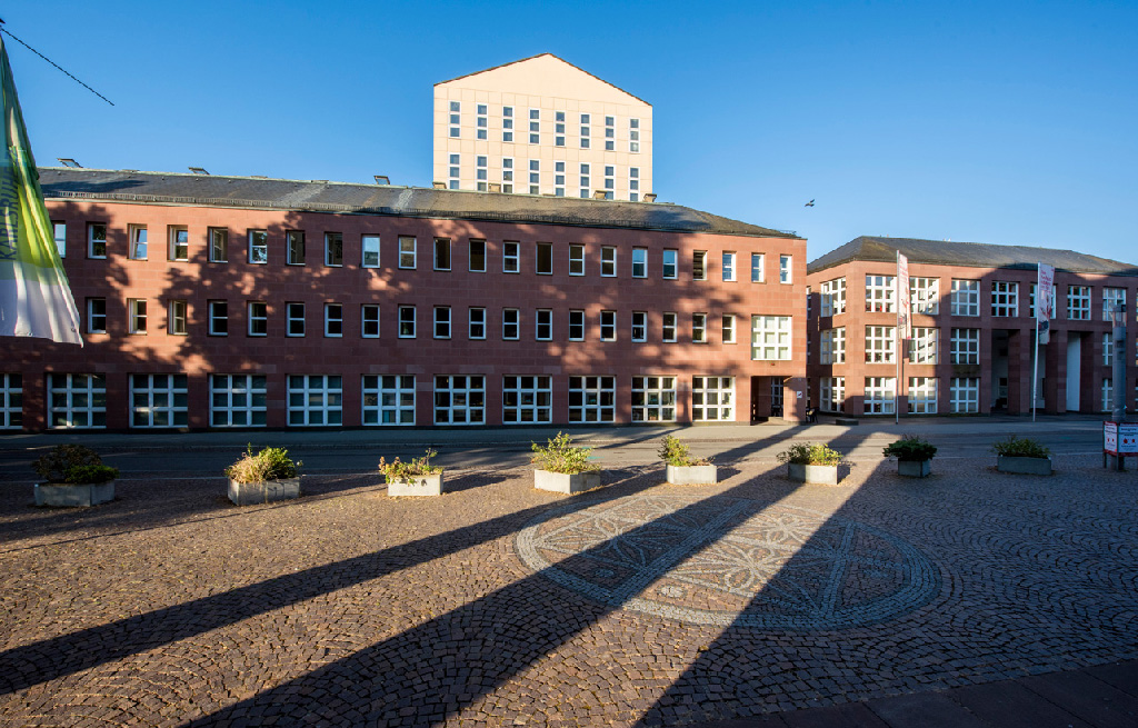 Zu sehen ist ein Bild von der Frontfassade der Badischen Landesbibliothek. Das Gebäude liegt im nachmittäglichen Schatten.