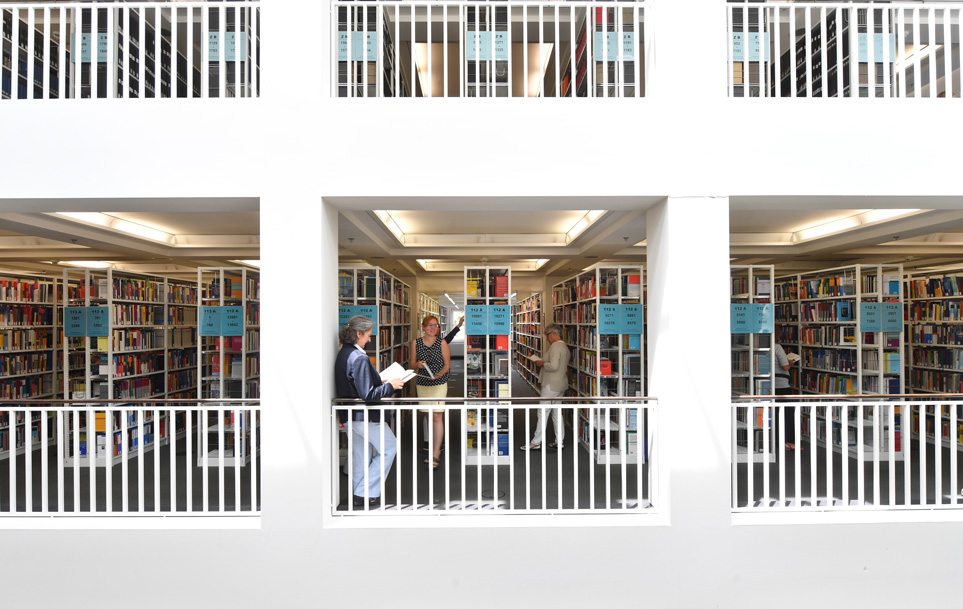 Zu sehen ist das offene Magazin der Badischen Landesbibliothek. Nutzerinnen und Nutzer sind beim selbständigen Abholen von Literatur zu sehen. 