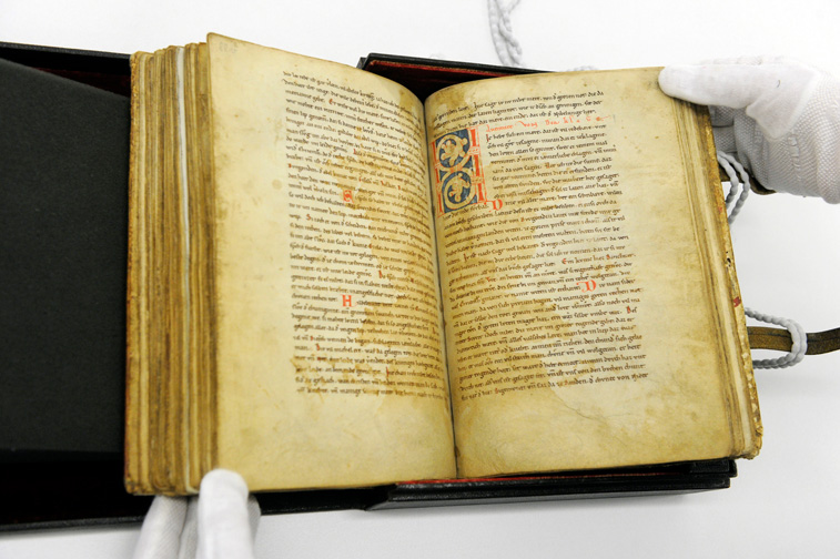 Das Bild zeigt die aufgeschlagene Handschrift C des Nibelungenlieds, die von einem Mitarbeiter mit Handschuhen gehalten wird. 