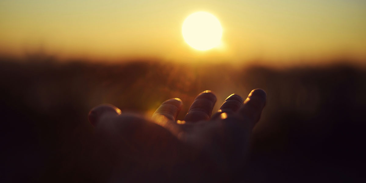 Eine Hand streckt sich in Richtung aufgehender Sonne.