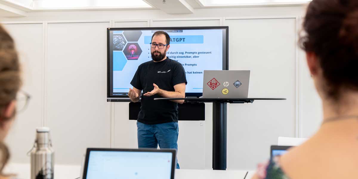 Auf dem Foto ist Workshopleiter Julius Link in der Lernwerkstatt abgebildet. Er steht vor einem TV-Screen, auf dem eine Infofolie zu ChatGPT zu sehen ist.
