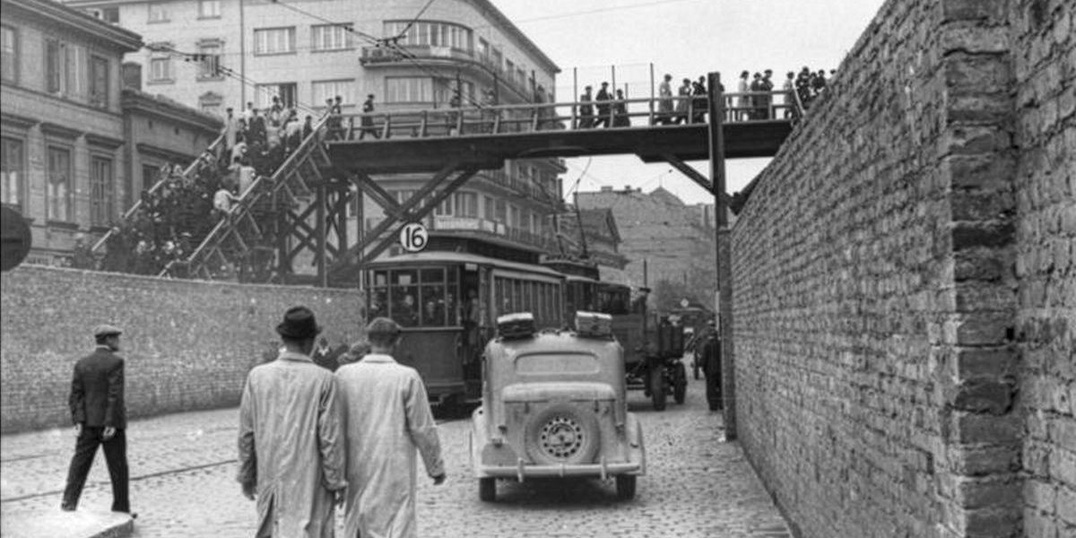 Zu sehen ist eine alte Fotografie des Warschauer Ghettos. Menschen gehen auf Straße über die Brücke, die zwei Ghetto-Bereiche miteinander verbindet.