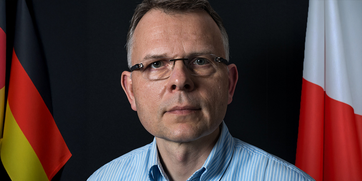 Portraitfoto von Prof. Dr. habil. Krzysztof Ruchniewicz, links ist die deutsche Flagge zu sehen, rechts die polnische Flagge.