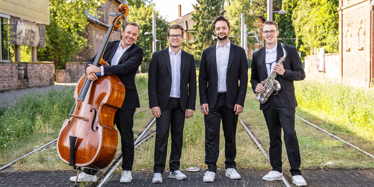 Foto der Gruppe „Salty Tunes“: Die vier Musiker stehen auf Straßenbahnschienen und halten Instrumente in den Händen.