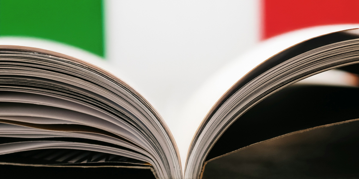 Zu sehen ist ein aufgeschlagenes Buch von der Seite. Im Hintergrund sind die italienischen Farben zu sehen.