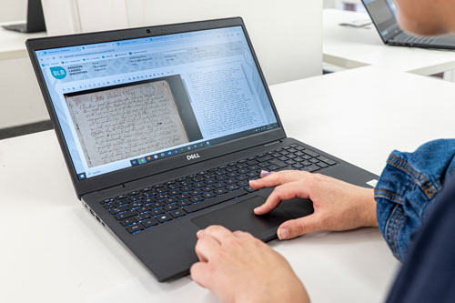 Der Bildschirm eines Laptops zeigt die Benutzeroberfläche der Digitalen Sammlungen der BLB. Rechts ist das historische Dokument – hier eine Brief – abgebildet, links der transkribierte Text.