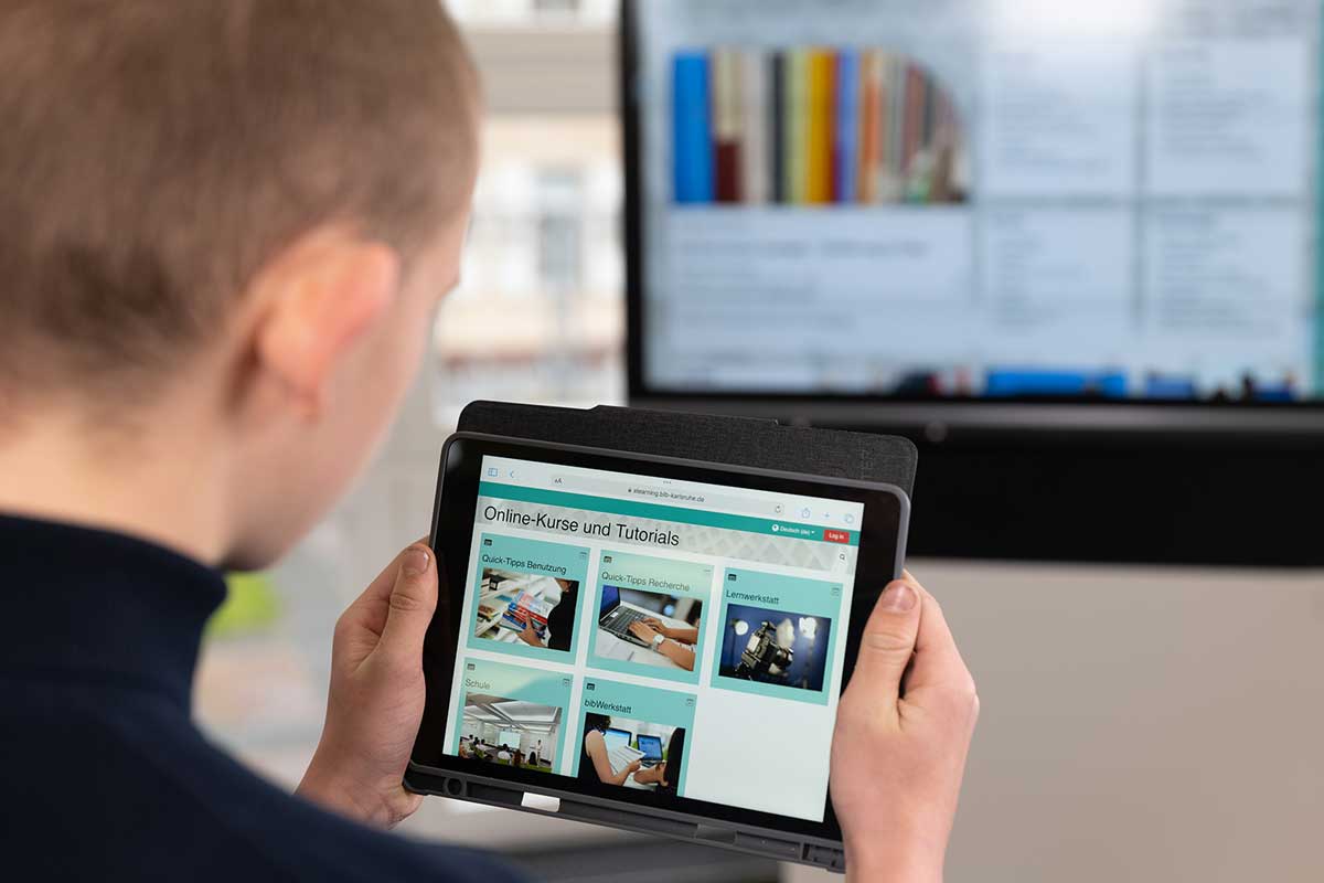Person mit Tablet in den Händen; Bildschirm zeigt Moodle-Startseite