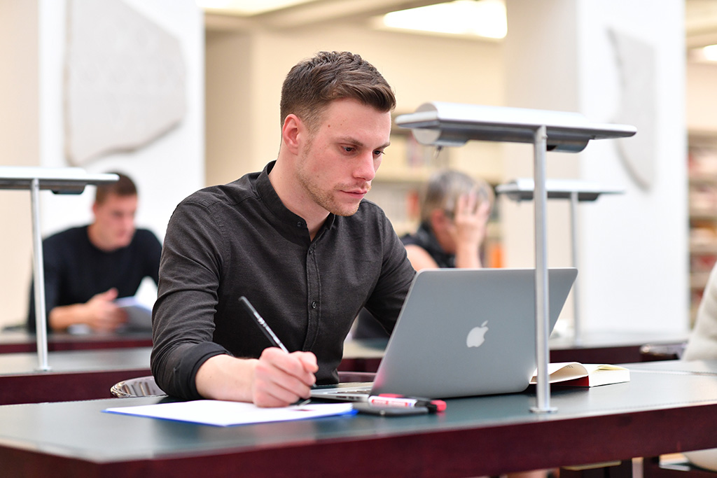 Das Bild zeigt einen Nutzer mit seinem Laptop an einem Arbeitsplatz im Lesesaal der Badischen Landesbibliothek.