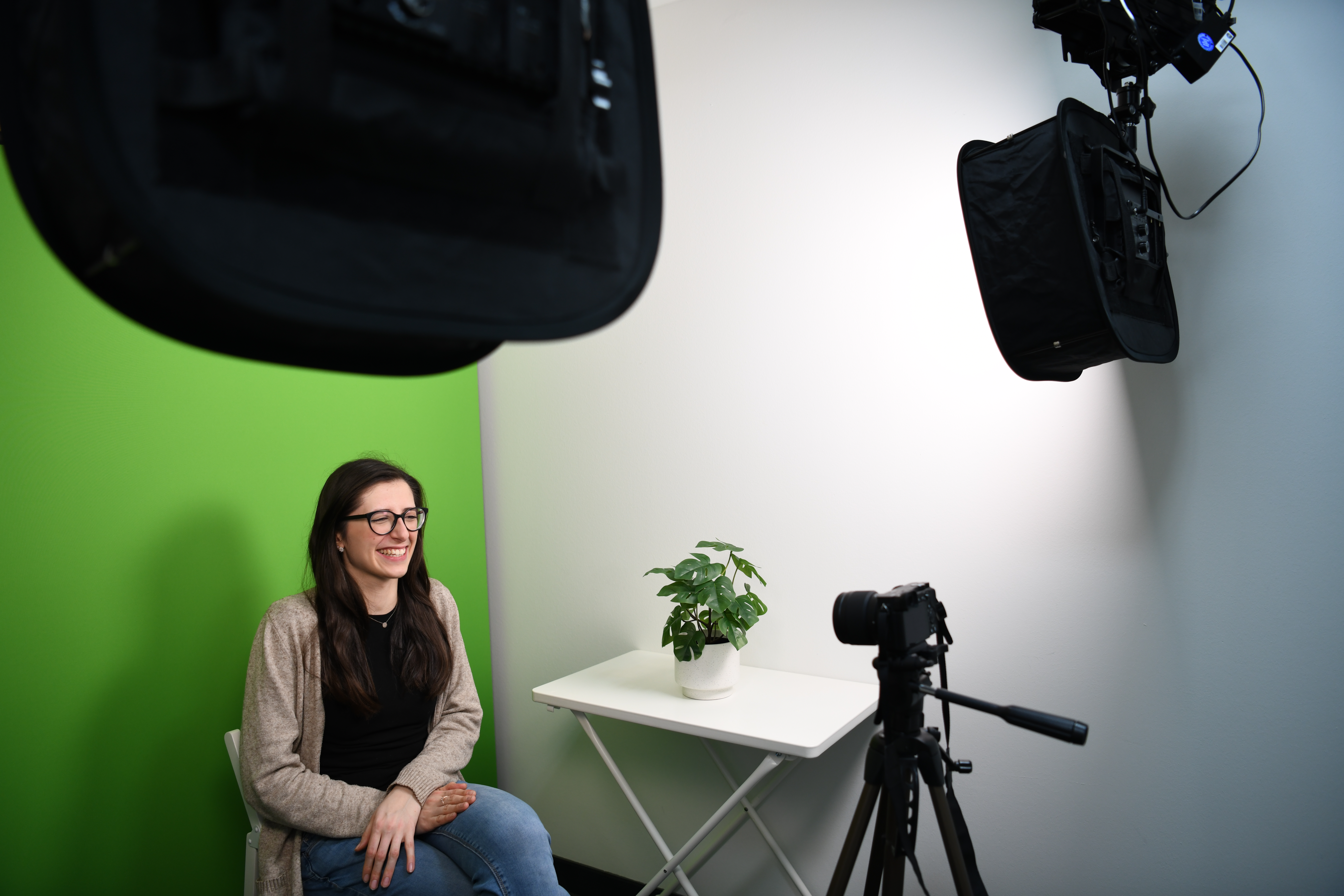 Zu sehen ist eine junge Frau, die im Media Studio der Lernwerkstatt vor einem Greenscreen von einer Kamera aufgenommen wird. 
