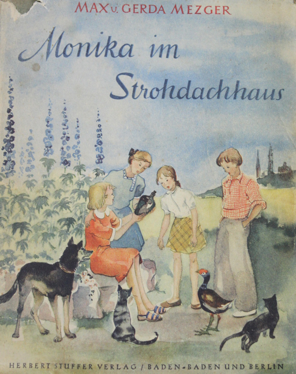 Gezeigt wird der Schutzumschlag des Kinderbuches „Monika im Strohdachhaus“ von Max und Gerda Mezger. Es erschien im Verlag von Herbert Stuffer im Jahr 1941. Zu sehen sind vier Kinder, umringt von Tieren, vor einer Kulisse aus Rittersporn. Eines der Kinder zeigt den anderen eine verkorkte Flasche.