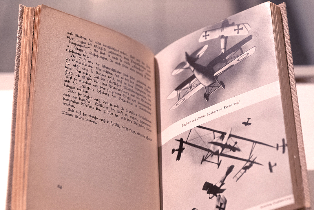 Aufgeschlagenes Buch mit zwei Darstellungen kämpfender Flugzeuge (rechts)