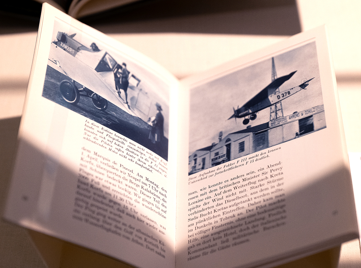 Aufgeschlagenes Buch mit Schwarz-Weiß-Fotografien von ins Flugzeug einsteigenden Pilotinnen (links) sowie einer fliegenden Fokker (rechts)
