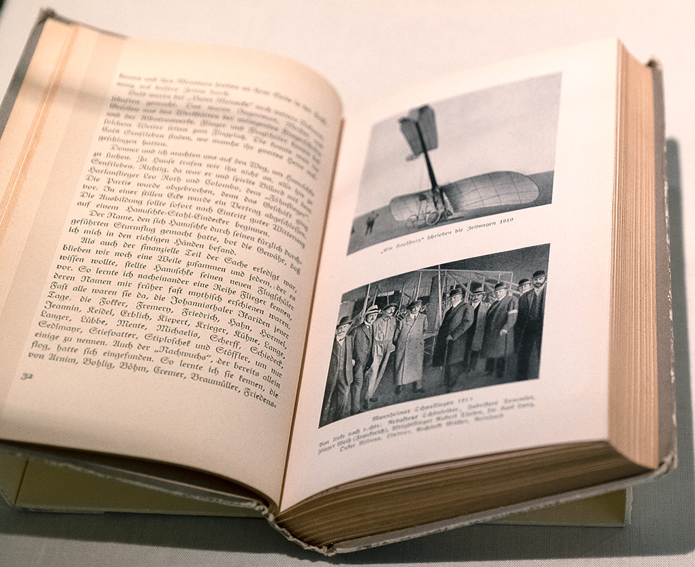 Geöffnetes Buch mit zwei Schwarz-Weiß-Abbildungen: 1. Gleitflugzeug, 2. Gruppenfoto
