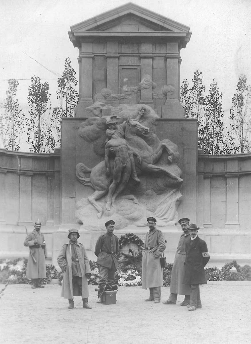 Schwarz-weiße Fotografie, die eine Gruppe Männer, darunter Soldaten, vor dem Grabmal für die gefallenen deutschen Soldaten, zeigt.