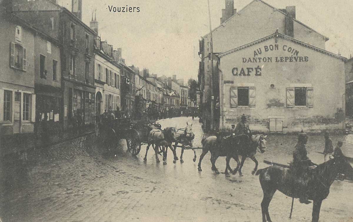 Schwarz-weiße Fotografie, die Soldaten auf Pferden und Kutschen, in einer Schlange, auf einer Straße in Vouziers zeigt.