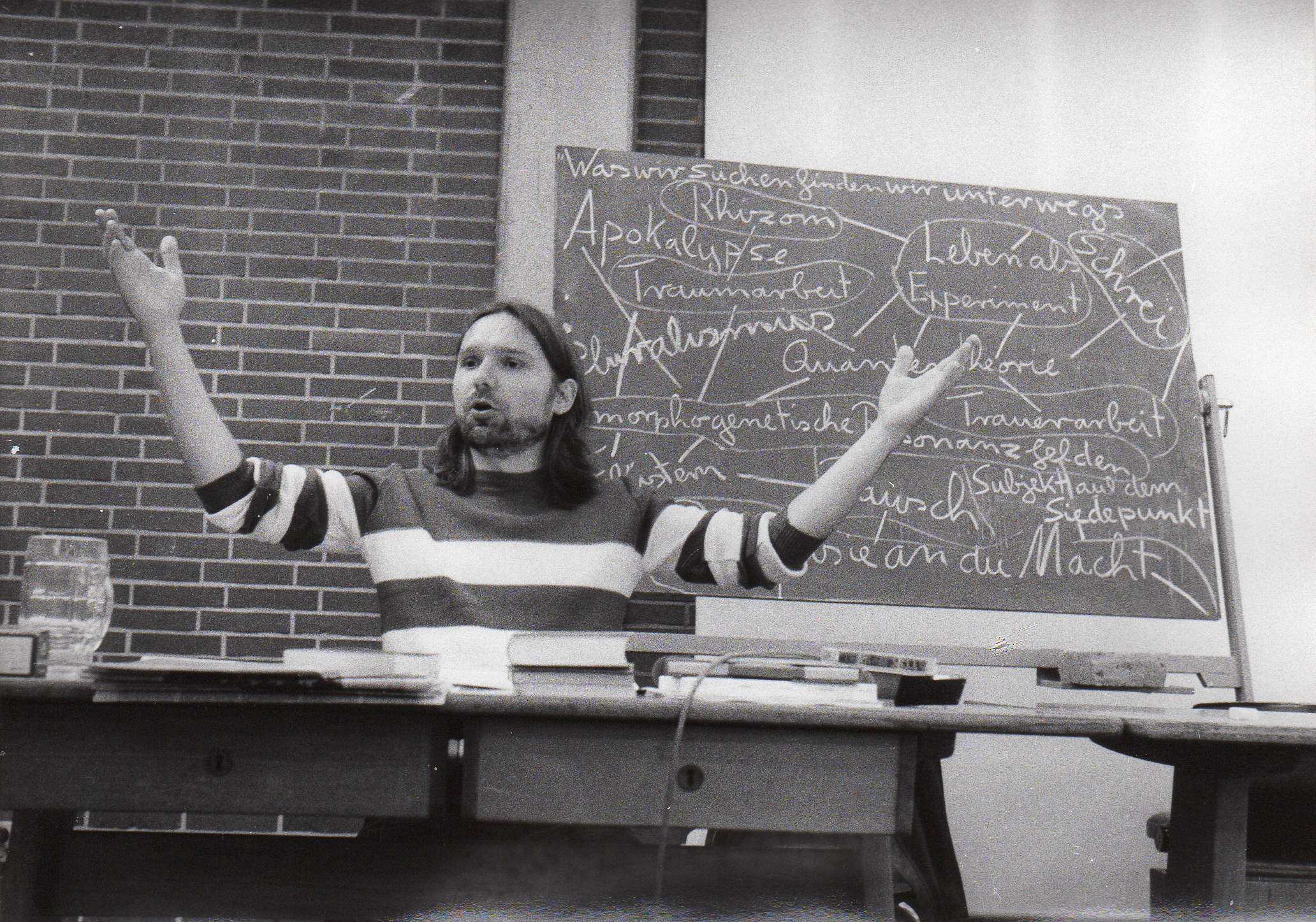 Joachim Krebs beim lehren, seine Arme sind erhoben, im Hintergrund eine vollgeschriebene Tafel.
