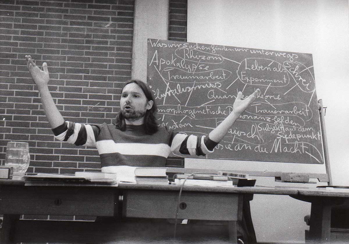 © Badische Landesbibliothek Joachim Krebs beim lehren, seine Arme sind erhoben, im Hintergrund eine vollgeschriebene Tafel.