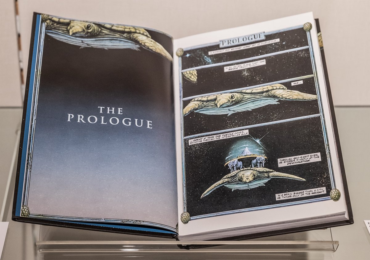 Das Bild zeigt ein aufgeklapptes Buch. Auf der linken Seite lassen sich die englischen Worte „The Prologue“ lesen, auf der Rechten ist eine große Schildkröte, die durch das Weltall schwebt, zu erkennen. Auf ihrem Rücken befinden sich zwei Elefanten, wiederrum tragen diese eine Erdplatte mit einem großen Berg auf ihren Rücken.
