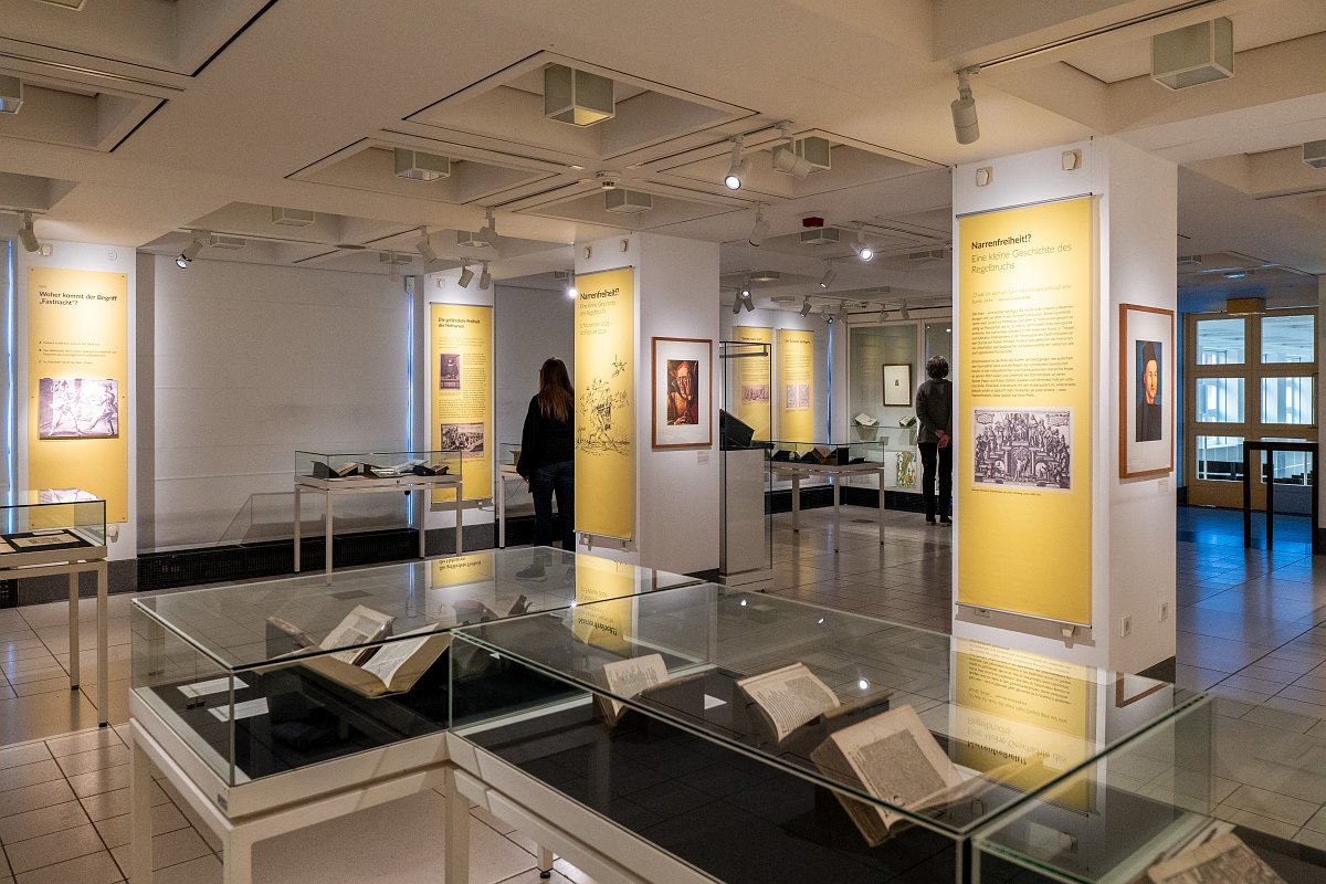 Das Foto zeigt eine Übersicht des Ausstellungssaals mit Buchvitrinen und Saalfahnen.