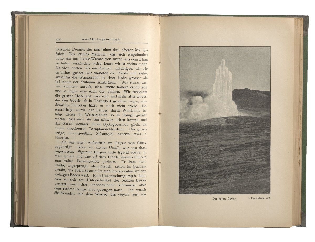 Zu sehen ist ein aufgeklapptes Buch, auf der rechten Seite ist eine Fotografie abgebildet, die den Ausbruch eines Geysirs zeigt. 