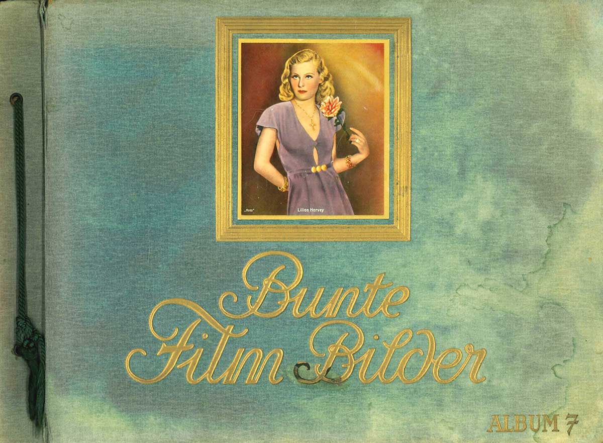 Der Vorderdeckel des Albums ist mit türkisfarbenem Stoff bezogen. Aufgeklebt in den vorgeprägten breiten Goldrand ist ein Bild von Lilian Harvey im lilafarbenen Kleid und mit einer Rose in der linken Hand.