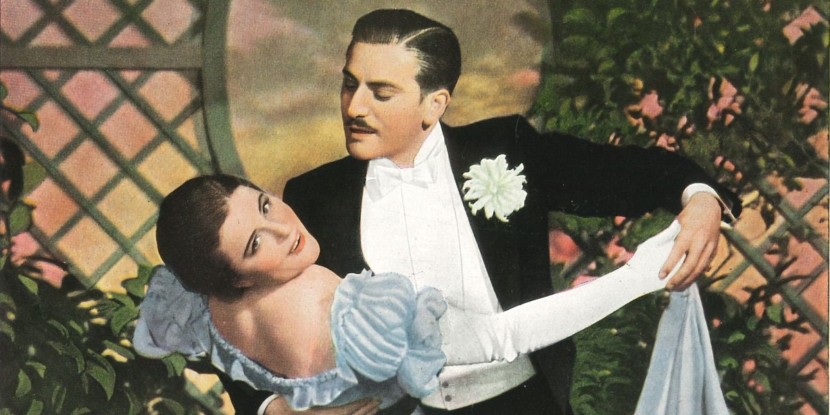 Farbaufnahme aus dem Tonfilm "Maskerade" mit Paula Wessely und Adolf Wohlbrück als tanzendem Paar vor einem Rosengitter.