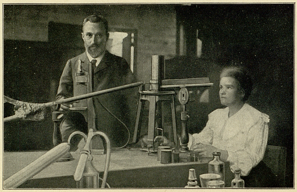 Die Abbildung zeigt Pierre und Marie Curie in ihrem Labor. Pierre steht hinter einem Labortisch, während Marie an dem Tisch mit Forschungen beschäftigt ist. 