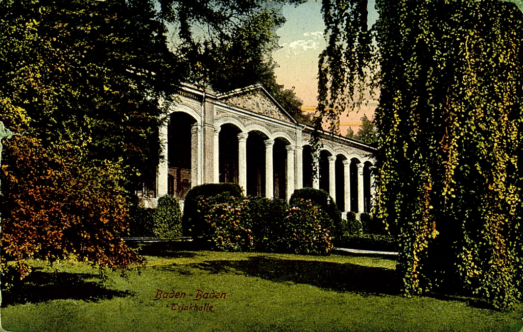 Das Bild zeigt eine kolorierte Postkarte mit der Teilansicht der Schaufassade der Trinkhalle Baden-Baden samt vorgelagerter Parkanlage. 