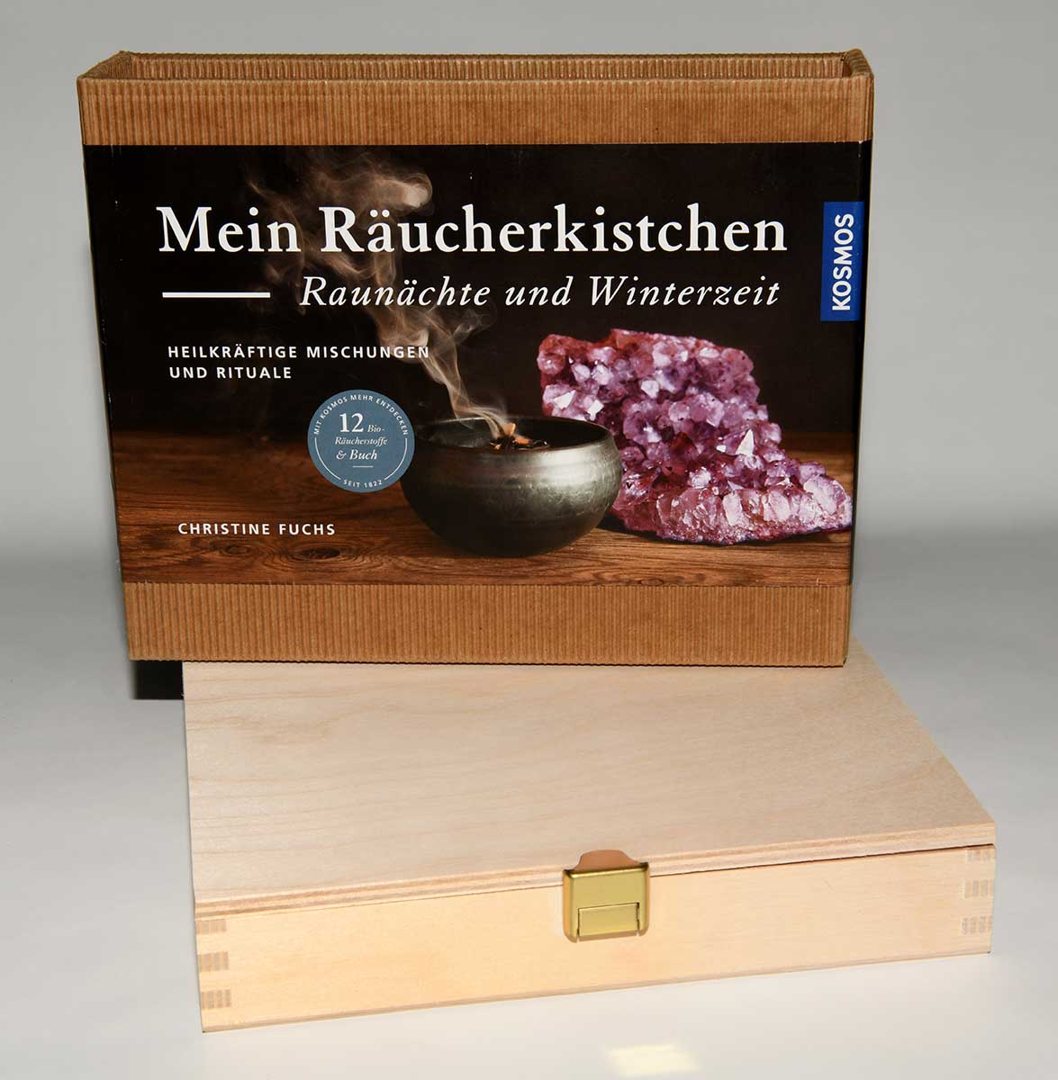 Holzkiste mit aufgesetztem Karton mit der Aufschrift 'Mein Räucherkistchen Raunächte und Winterzeit' und einem Bild von einer rauchenden Schale neben einem Amethyst-Kristall.