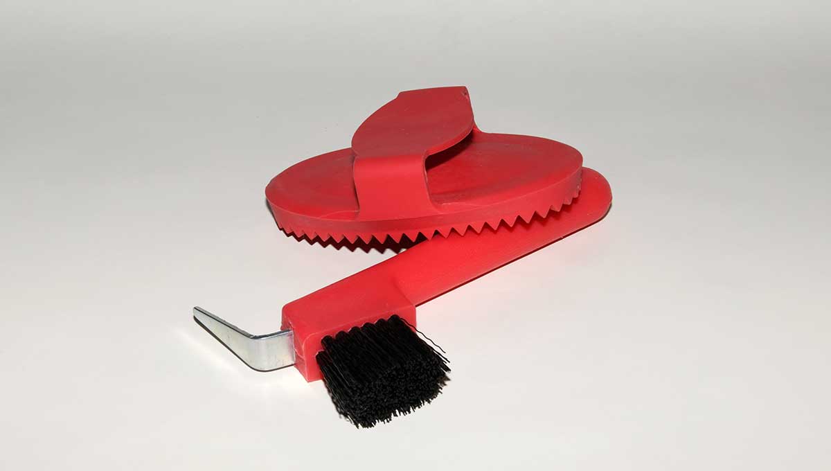 Zu sehen ist ein roter Pferdestriegel mit Griff und Hufauskratzer mit Metallspitze und Borsten.