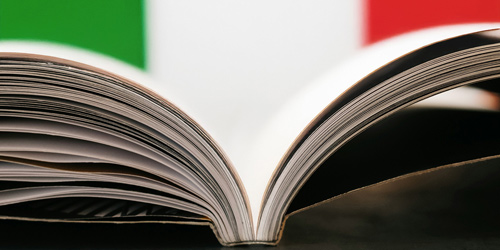 Zu sehen ist ein aufgeschlagenes Buch von der Seite. Im Hintergrund sind die italienischen Farben zu sehen.