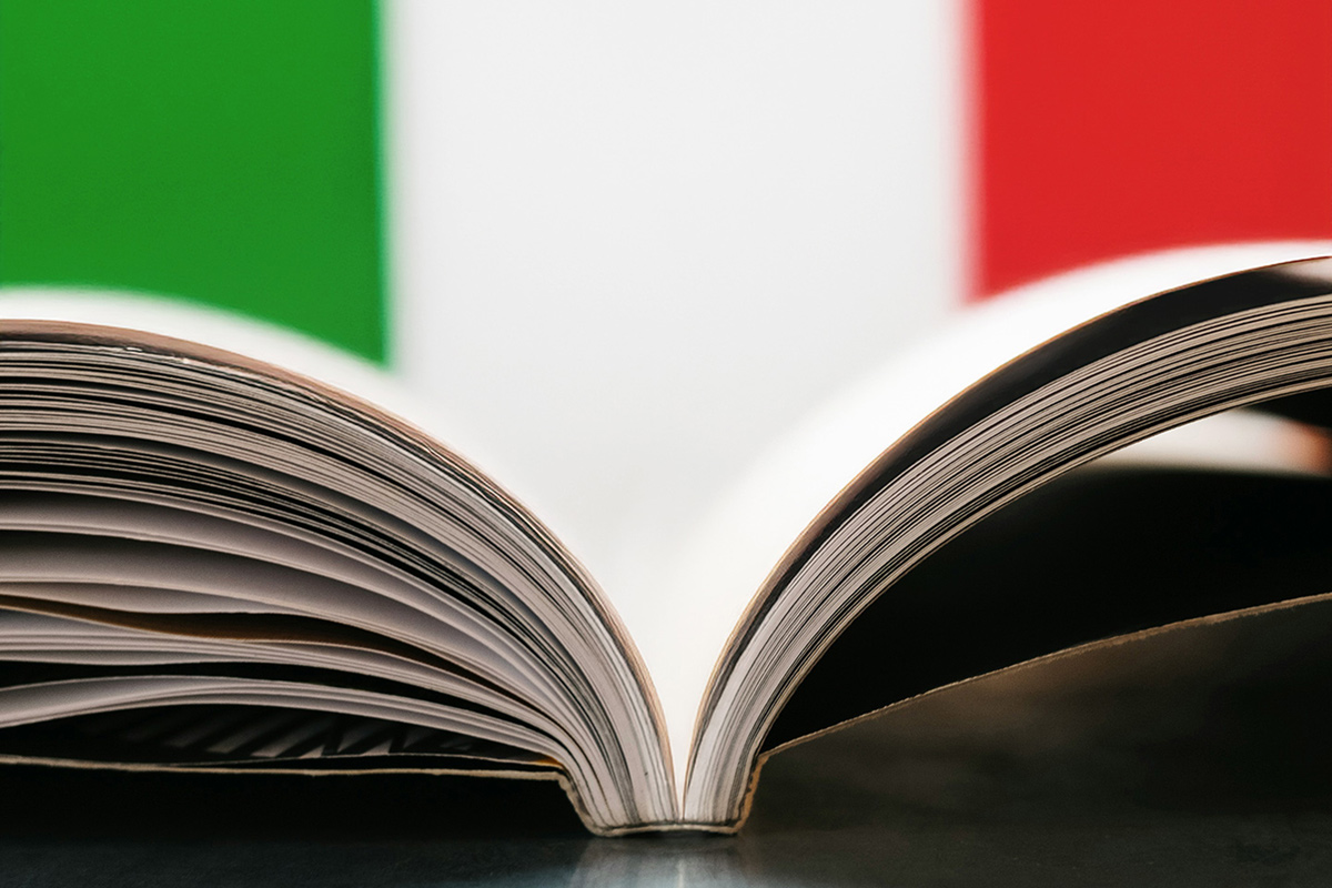 Zu sehen ist ein aufgeschlagenes Buch von der Seite. Im Hintergrund sind die italienischen Farben zu sehen.