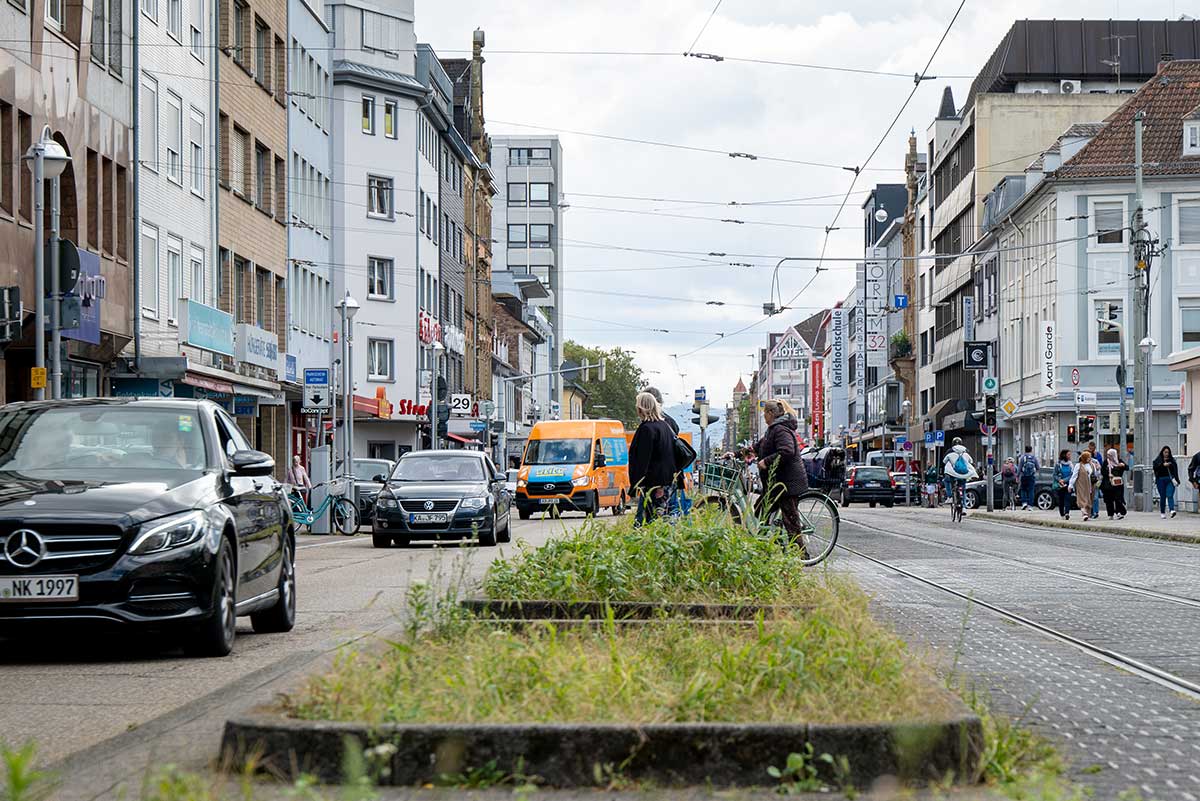 Straßenszene mit Autos, Fußgängerinnen und Radfahrerinnen.